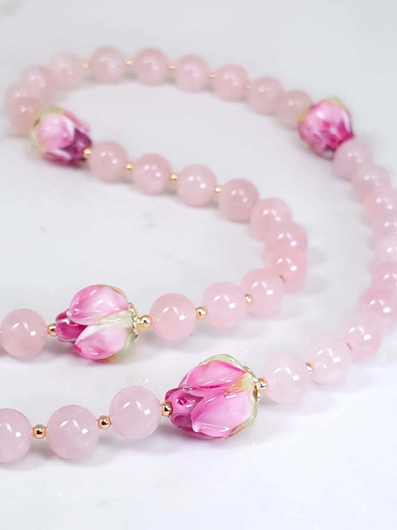 Full view of rosary beads featuring Pink Rose Quartz and rosebud lamp-work flower beads, showcased on a white table backdrop.