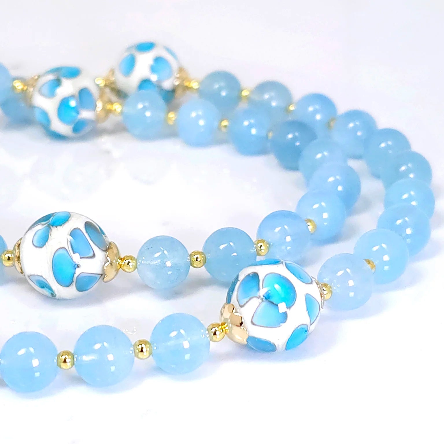 Detailed view of rosary beads crafted from Blue Aquamarine with gold-filled round wire, showcased on a white table.