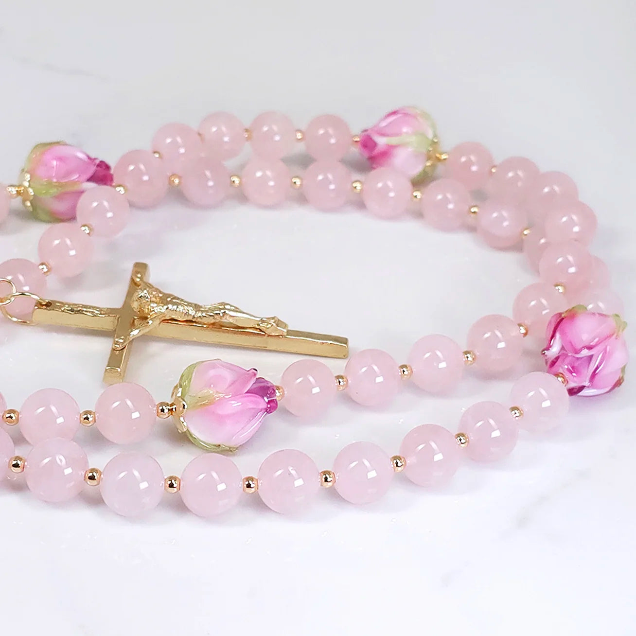 Rosary displaying Pink Rose Quartz and unique rosebud lamp-work flower glass beads, spread out on a white table.