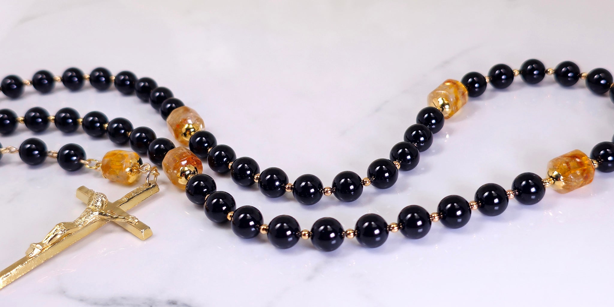 Black Onyx rosary with gold citrine gemstone focal beads and gold finding placed on top of a shiny table.