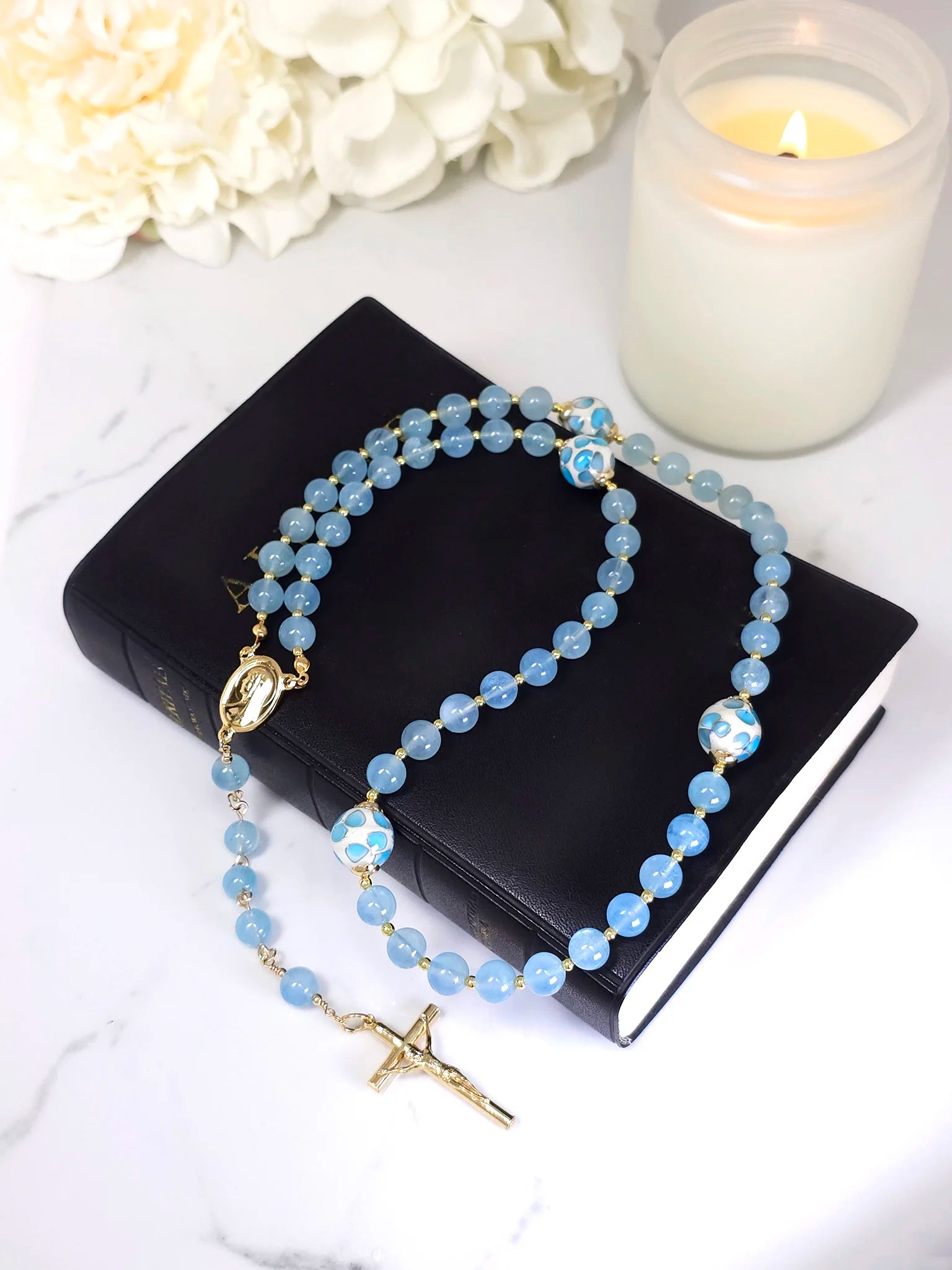 Rosary beads with Blue Aquamarine, elegantly complemented by gold-filled spacers and bead caps, displayed on a white table.