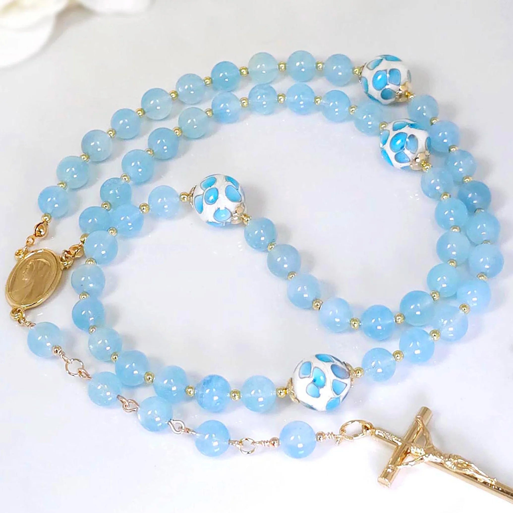 Rosary featuring delicate flower glass beads with a Gold-plated Crucifix pendant and Madonna rosary center, on a white table.