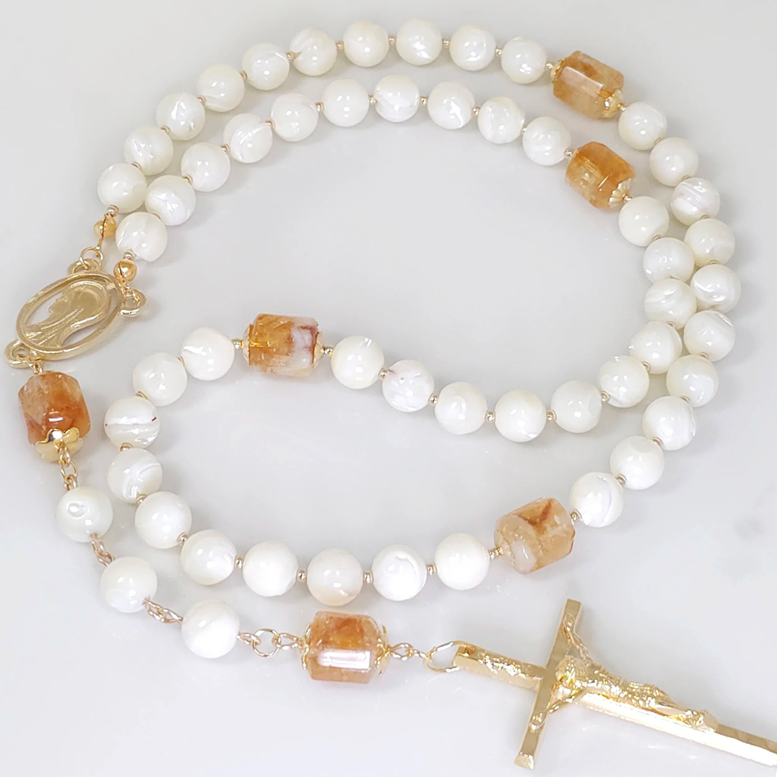 Elegant Mother of Pearl rosary with golden Citrine beads and a Gold-plated Crucifix, displayed on a white table.