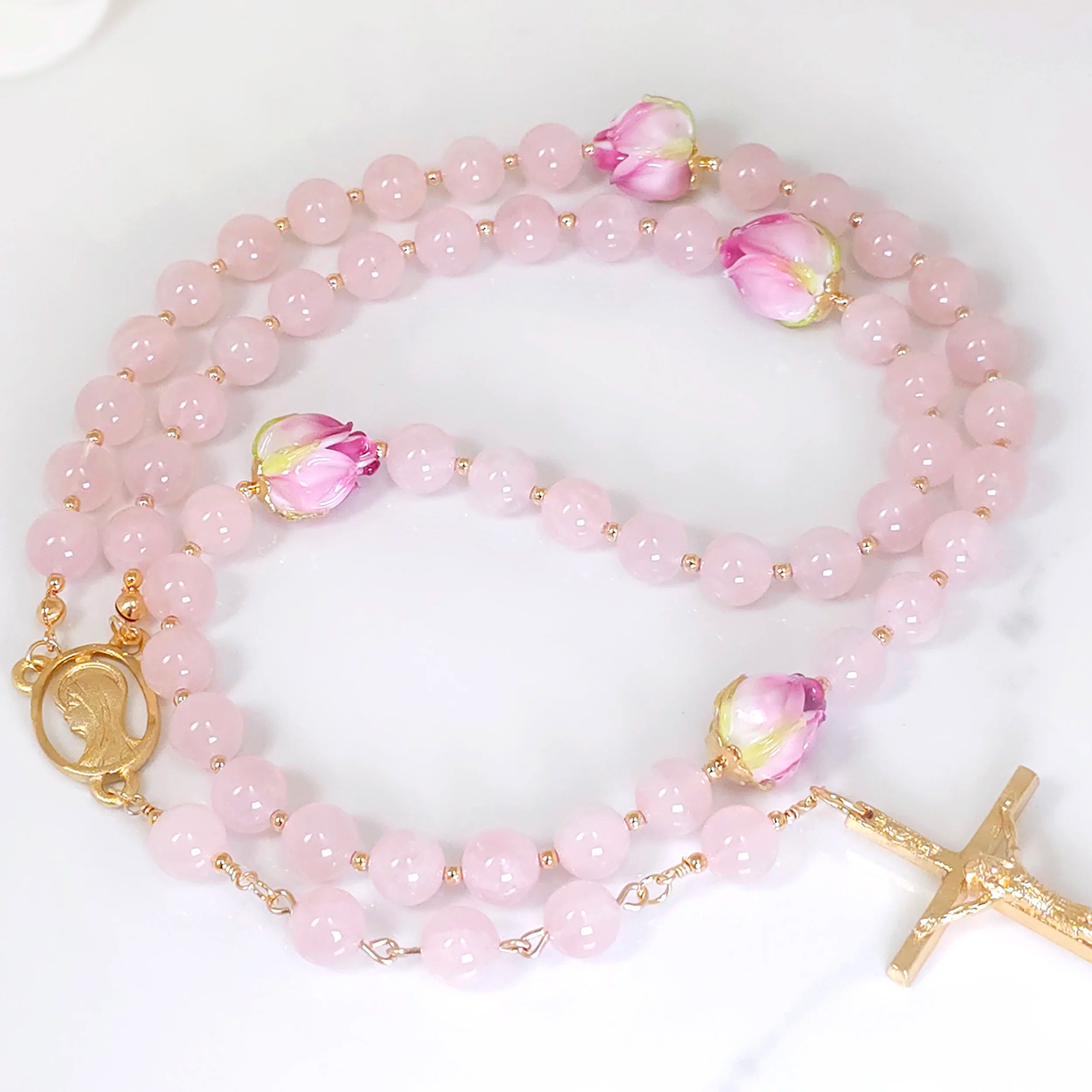 Close-up of Pink Rose Quartz rosary beads with gold-filled spacers, laid on a white table.