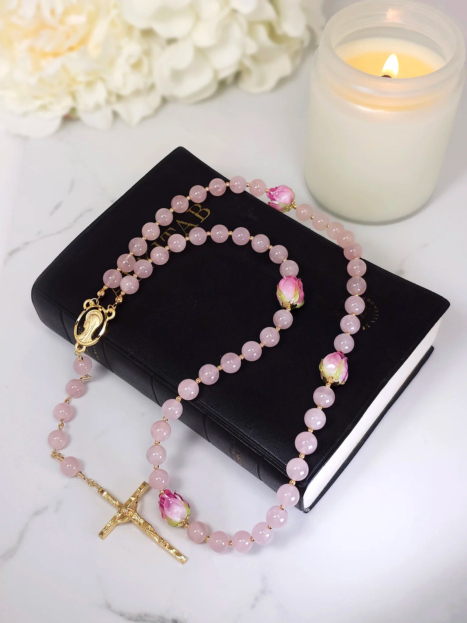 Rosary necklace emphasizing a gold-plated Madonna medal amidst pink quartz beads, draped on a white table.