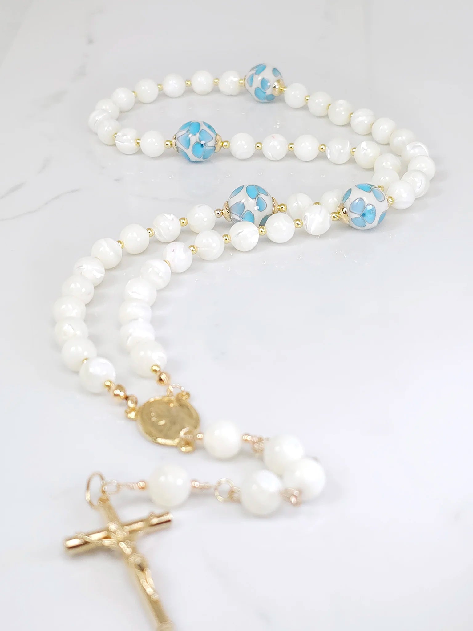Rosary adorned with little blue flower glass beads, complemented by a Gold-plated Madonna medal centerpiece.