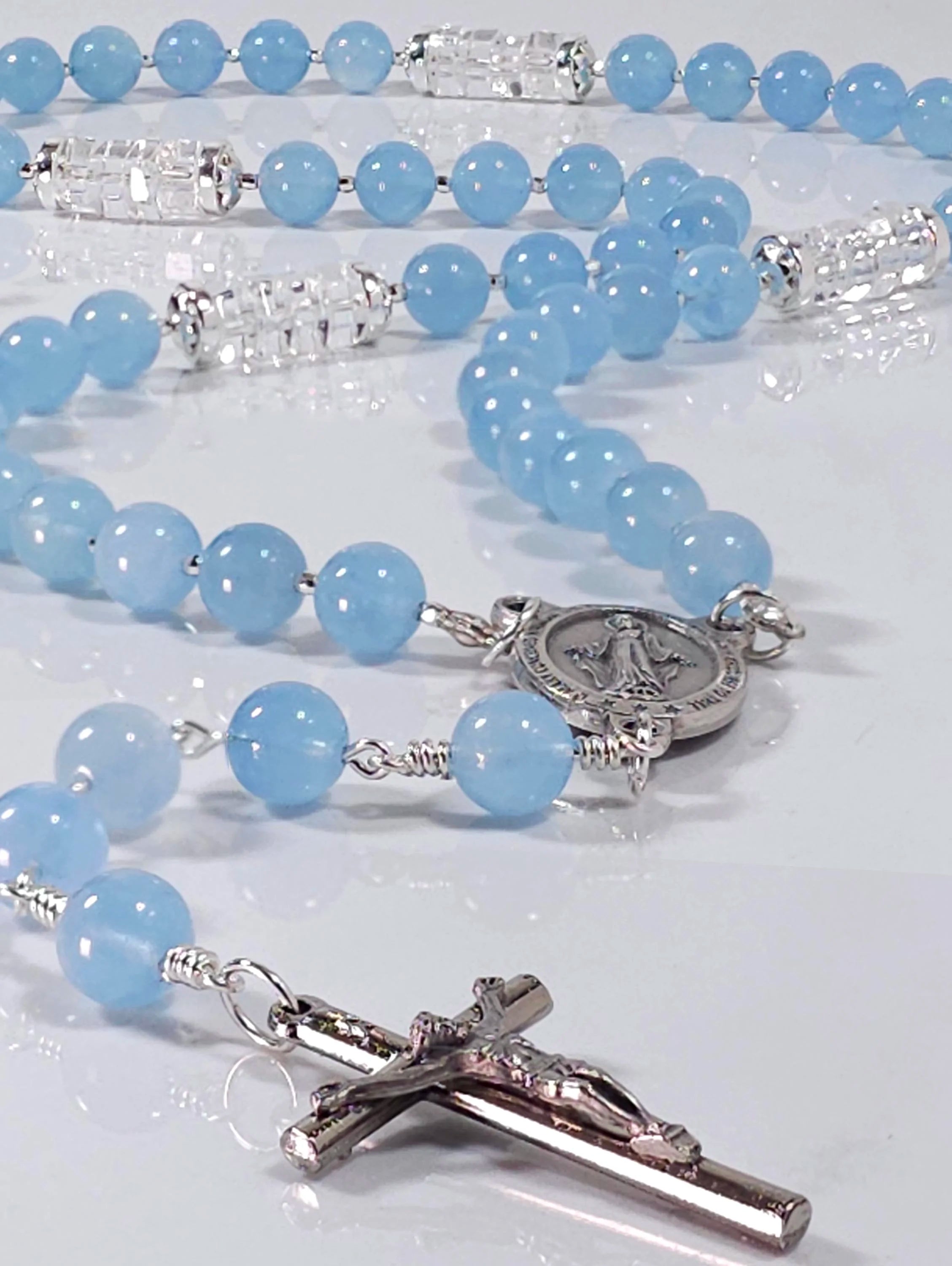 Heirloom quality blue catholic rosary adorned with sterling silver findings laying on white surface.