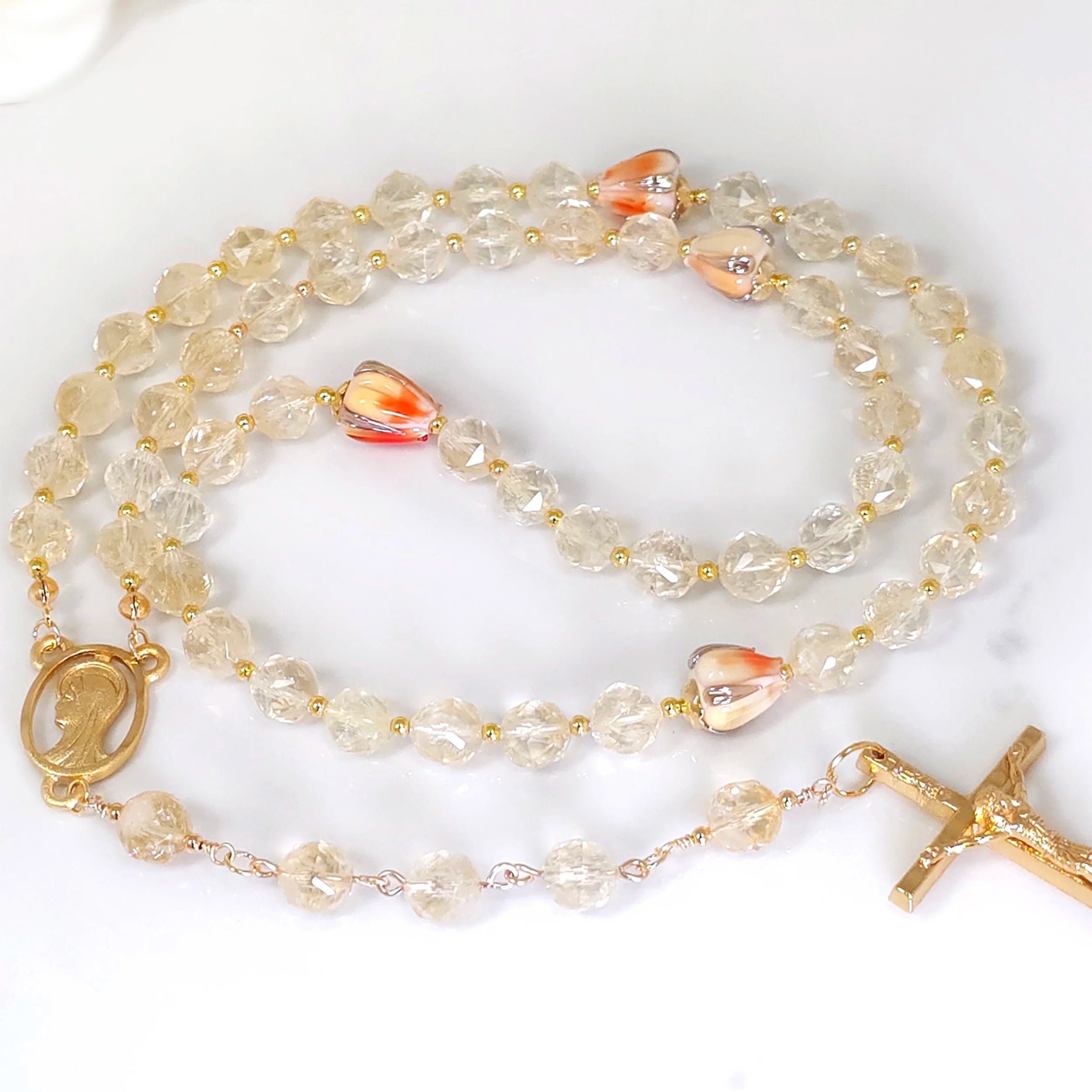 Rosary with gold citrine beads and orange floral lamp work accents with silver leaf, laid out on a table.