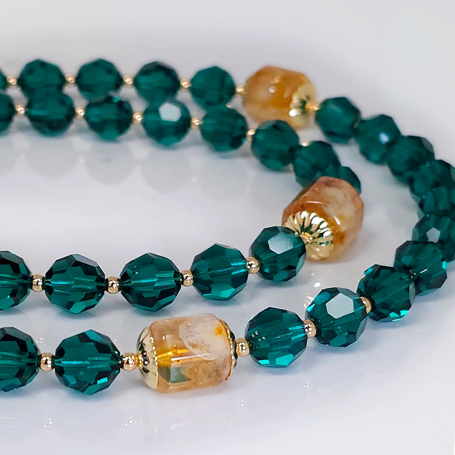 A close-up view of emerald rosary beads with Swarovski crystals, elegantly laid on a white table.