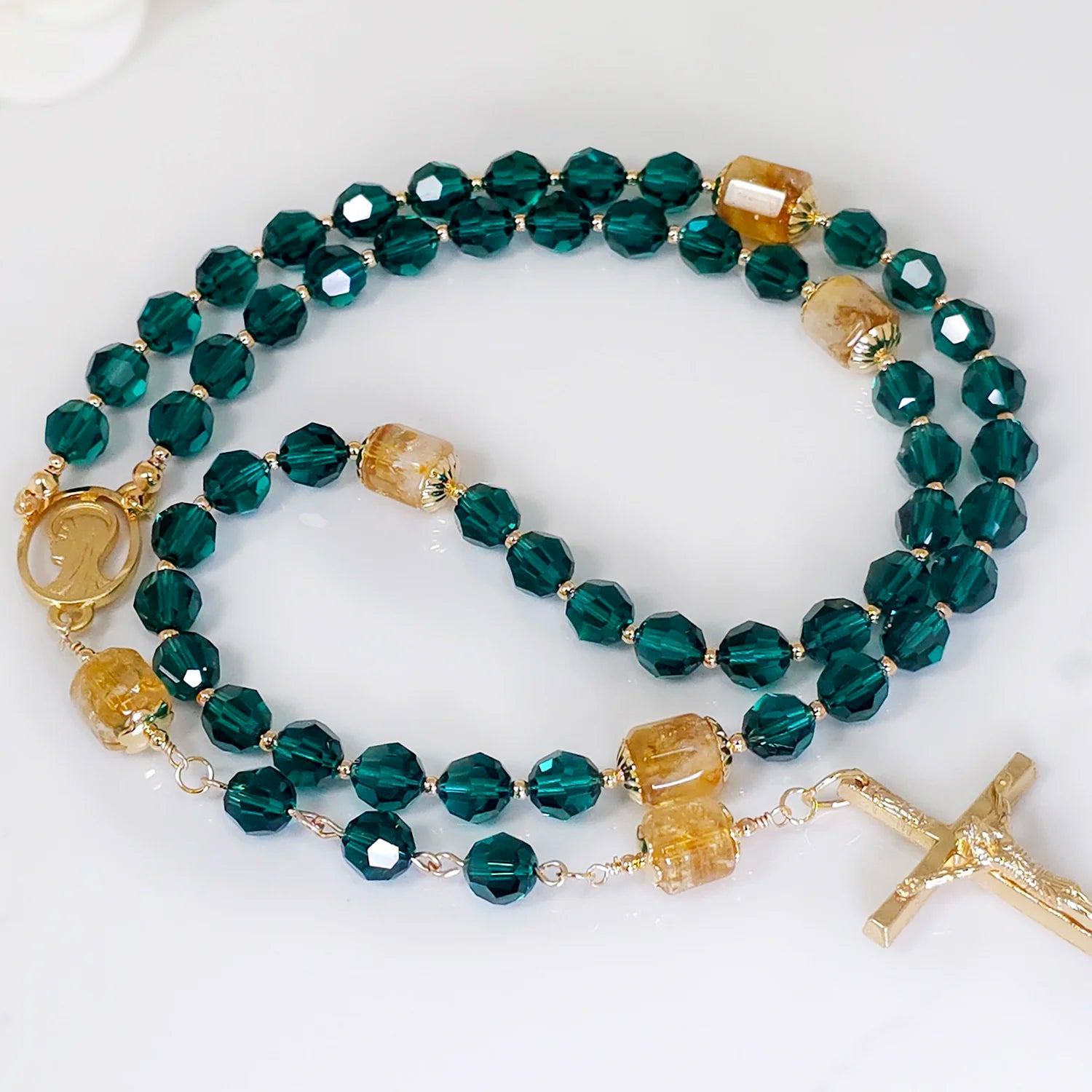 Five-decade rosary showcasing the deep hue of emerald beads, complemented by Golden Citrine accents, set on a white table.