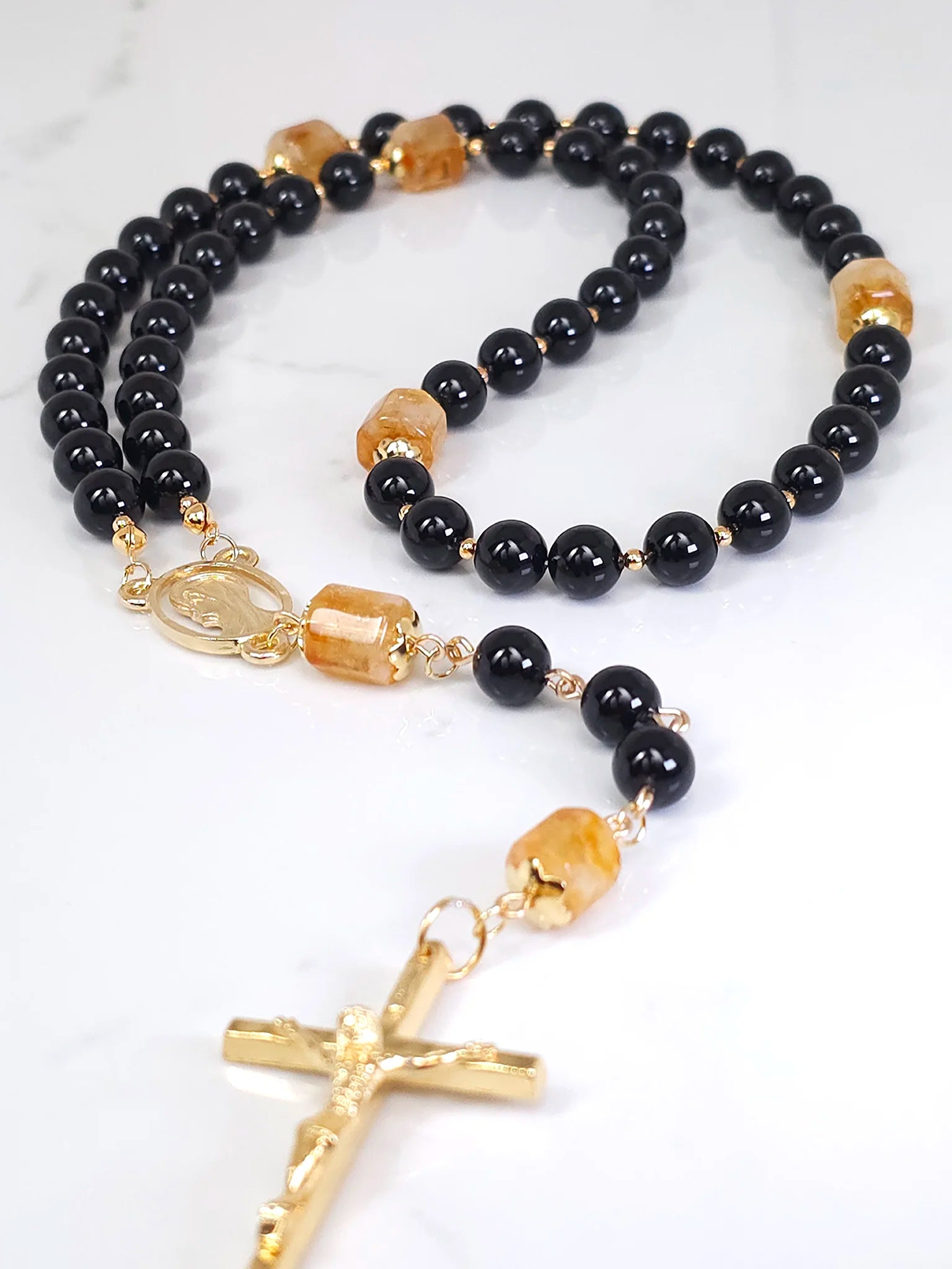 Unique rosary made from Black Onyx and Golden Citrine, accentuated by gold-filled bead caps, showcased on a white table.