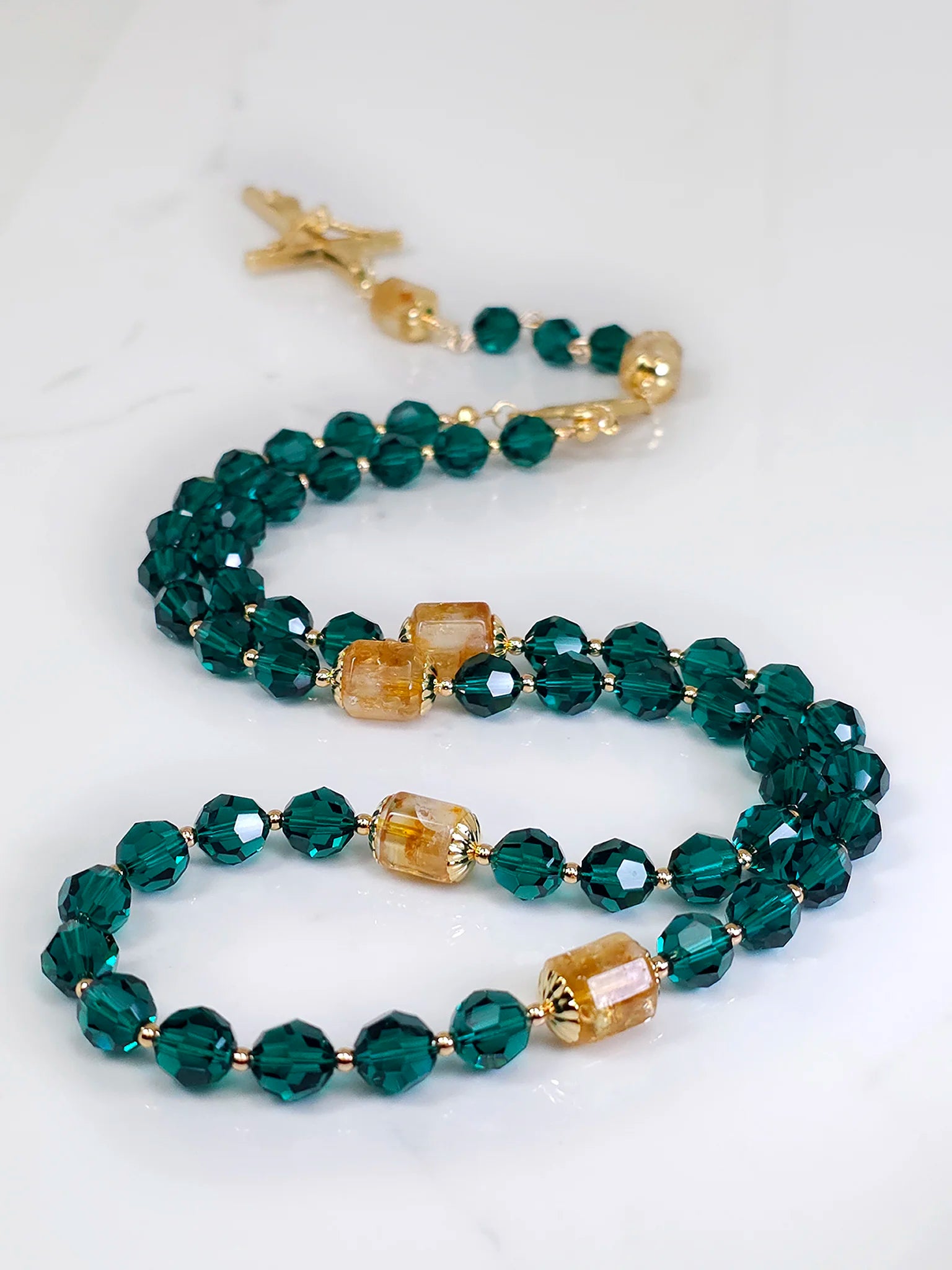 Delicate rosary design with green beads and gold details, artistically spread on a pristine white table.