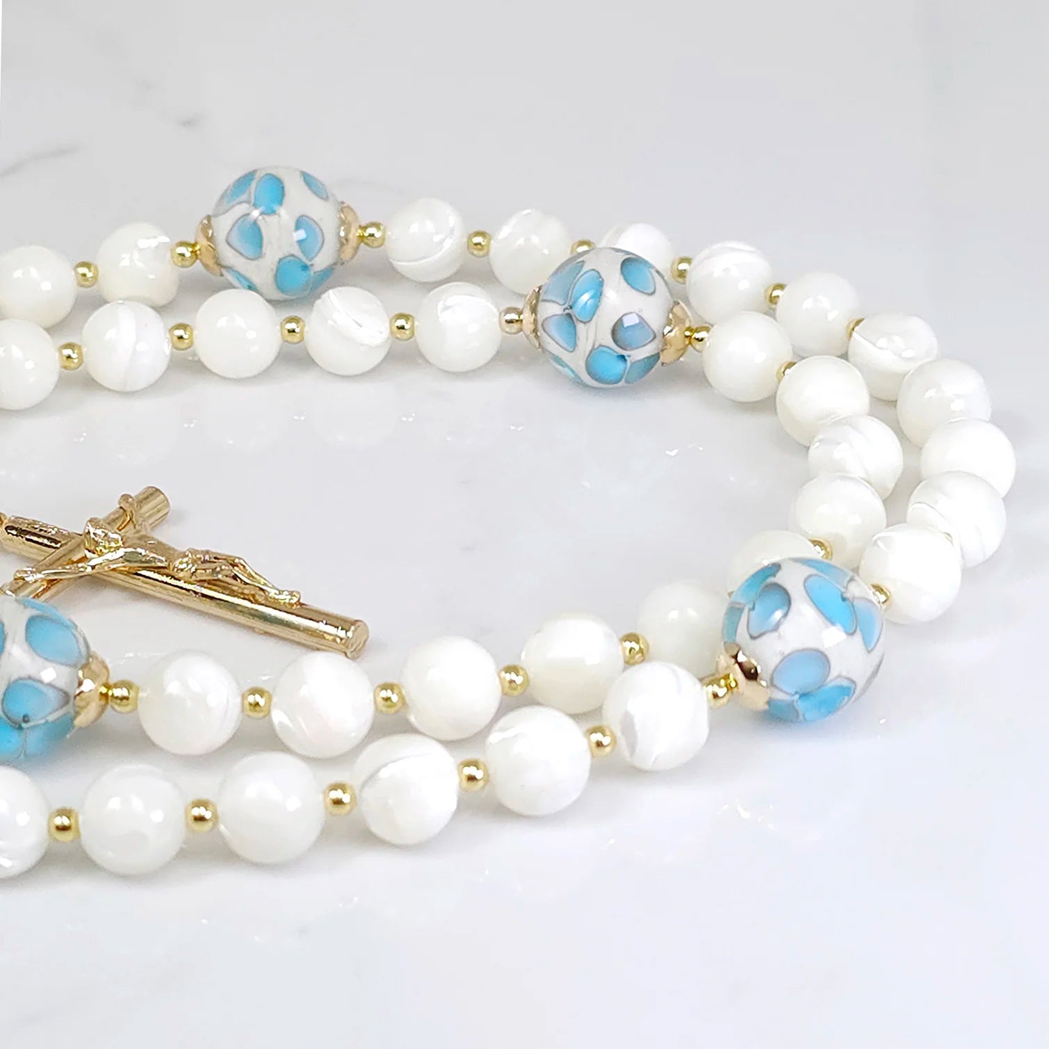 Catholic devotion rosary featuring White Mother of Pearl and little blue flower glass beads, displayed on a surface.