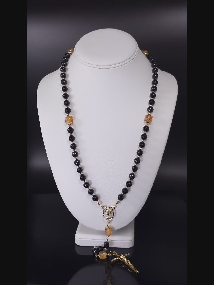Rosary beads crafted from Natural Black Onyx with a Gold-plated Crucifix pendant, presented on a white table.