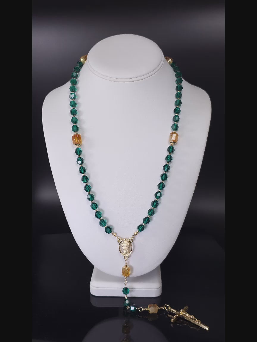 Green Emerald Crystal Catholic Rosary Beads with gold-plated Crucifix and Madonna centerpiece, resting on a white table.