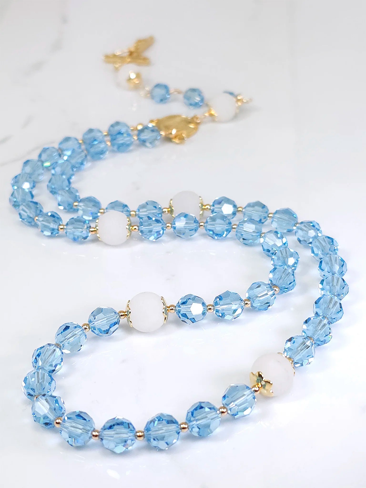 17.5-inch rosary necklace made of Blue Aquamarine Austrian Crystal with gold-filled bead caps and spacers.